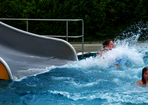 Das Ende einer Breitwellenrutsche in einem Schwimmbecken, in dem sich zwei Personen befinden.