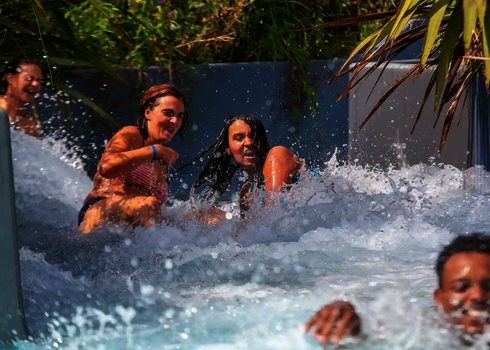 Drei junge Frauen rutschen lachend gemeinsam durch den Wildwasserfluss.