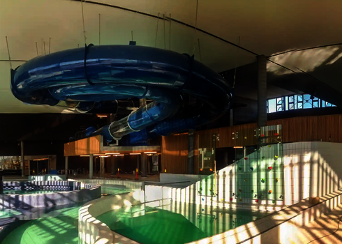 Teilansicht eines Schwimmbades, mit Blick auf eine blaue RR1400 Wasserrutsche, die von der Decke hängt.