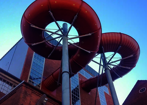 Blick von unten auf die rote Wasserrutsche und ihre Halterung an der Gebäudefassade.