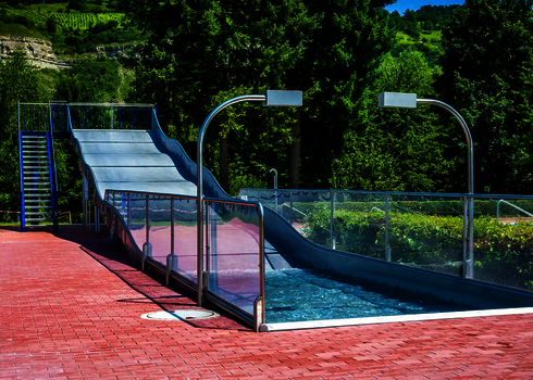 Eine Breitwellenrutsche mit blauer Treppe, vor einem grünen Berg mit Bäumen.
