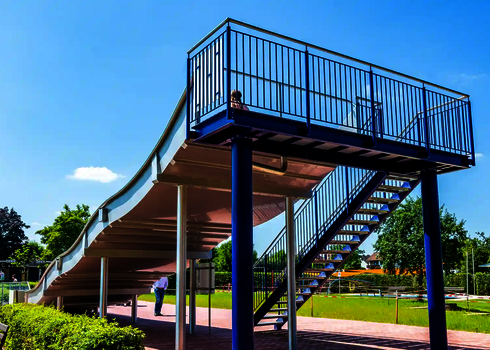 Blick vom hinten auf die Rückseite einer Breitwellenrutsche und die dazugehörige blaue Treppe.