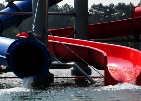Eine rote offene Rutsche und eine blaue geschlossene Rutsche enden in einem Wasserbecken.