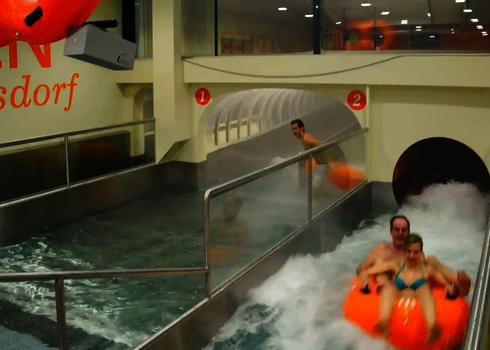 Two people slide on orange tyres through a double run-out with stainless steel pools.