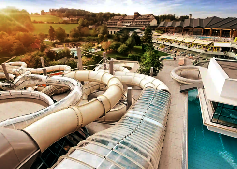 Blick auf den Außenbereich eines Wasserparks mit weißen Rutschen, im Hintergrund eine Hotelanlage.