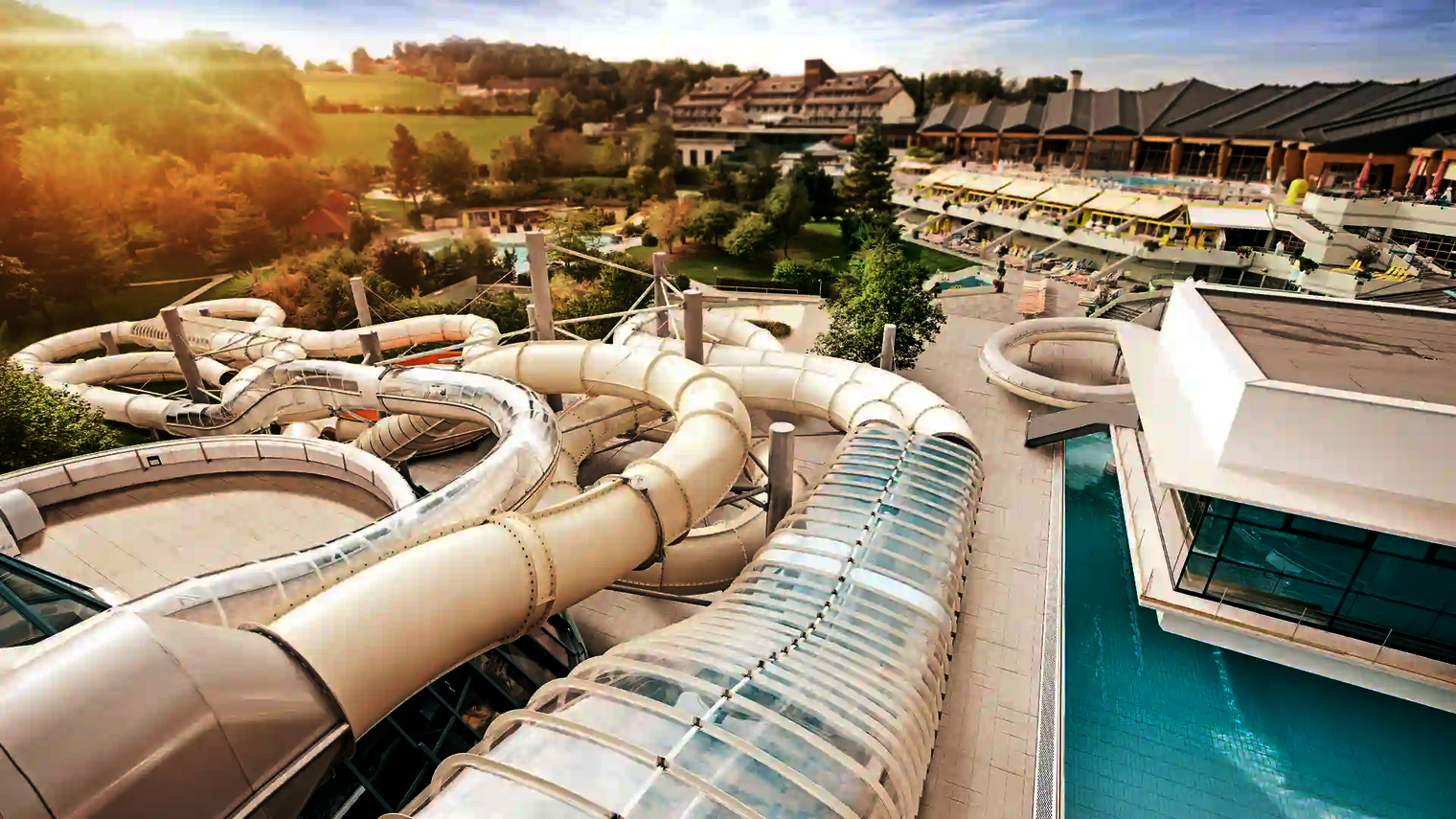 Blick auf den Außenbereich eines Wasserparks mit weißen Rutschen, im Hintergrund eine Hotelanlage.