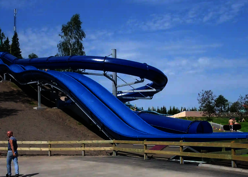 Eine gewellte Harakiri Freizeitparkrutsche in blau, getragen von Stützen entlang eines Hangs.