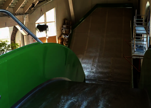 Grüne Sidewinder Wasserrutsche mit Wasserlauf und künstlicher Felslandschaft im Innenraum.