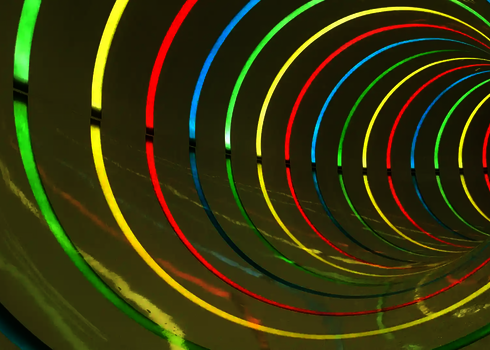 Innenansicht einer gelben Röhrenrutsche mit farbenfrohen Lichteffekten in Form von Ringen.