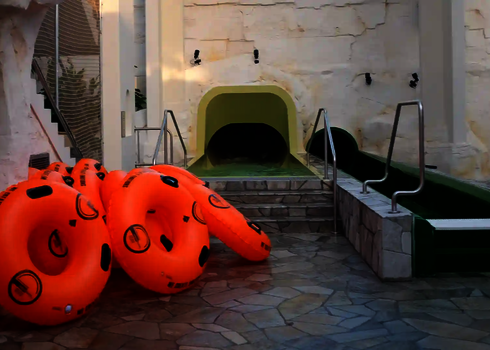 Mehrere orangefarbene Rutschreifen liegen bereit vor dem Einstieg in eine grüne Tunnelrutsche.