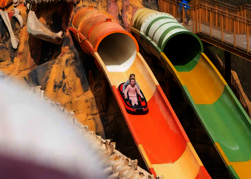 Zwei Personen in einem Boot rutschen auf einer Harakiri Rutsche in einem Dino-Freizeitpark.