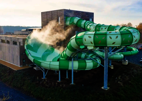 Außenansicht der grünen Lotus Reifenrutsche mit dampfendem Wasserparkbereich.