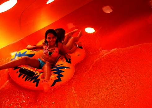 Zwei Kinder rutschen Rücken an Rücken in einem Rutschreifen in einem orangefarbenen Family Twister mit Tageslichteffekten.