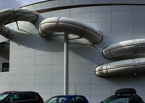 Weiße gedämmte Wasserrutsche in mehreren Bögen an der Außenwand eines modernen Bades.