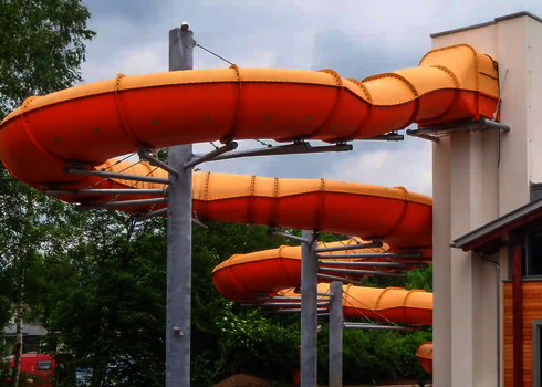 Die Reifenrutsche Family Twister führt in langgezogenen orangefarbenen Kurven an Stützpfeilern vorbei.