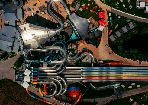 Vogelperspektive auf einen großen Wasserpark mit einer Edelstahl-Matracer Rutsche, einer Body Bowl und einer Urknall Wasserrutsche.