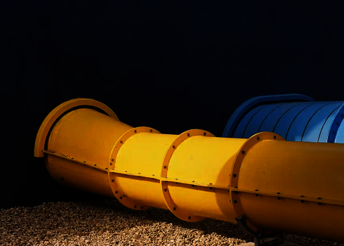 Gelbe und blaue Wasserrutsche durchdringen dunkelblaue Fassade nebeneinander.