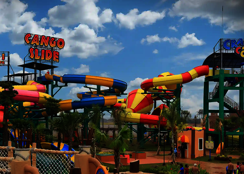 Freizeitpark mit mehreren Crazy Cone Rutschen, gelb-rote Trichter, grüne Tragstruktur, Palmen.