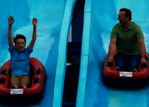 Vater und Sohn rutschen nebeneinander in zwei Rutschbooten die Harakiri Wasserrutsche herunter.