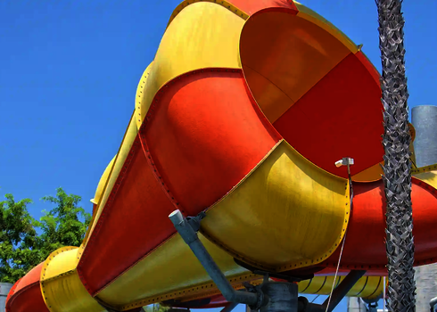 Nahaufnahme der gelb-orangenen Trichteröffnung der Crazy Cone Rutsche bei blauem Himmel.
