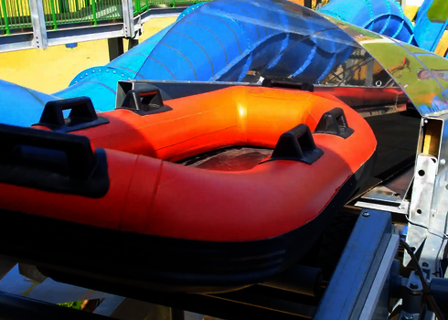 Rotes Schlauchboot auf einem Reifenlift, daneben eine blaue Wasserrutsche,