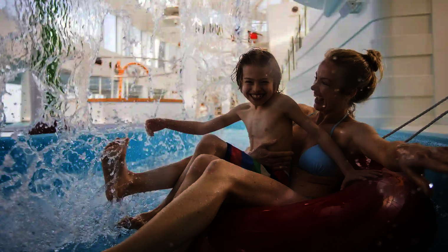 Mutter und Kind genießen eine Fahrt auf dem Lazy River mit Rutschreifen unter Wasserfall.