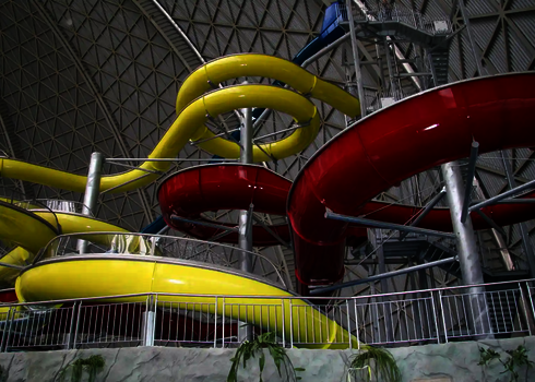Gelbe und rote Wasserrutschen winden sich in einer großen Indoor-Anlage.