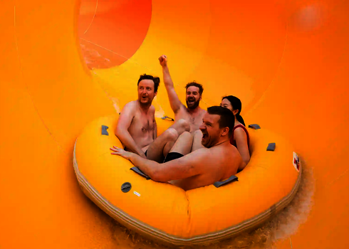 Vier Erwachsene rutschen mit Schwung durch den weiten gelben Trichter der Reifenrutsche RR2700.