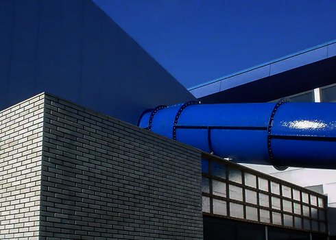 Blaue Wasserrutsche mit Schraubverbindungen führt aus einem modernen Bau heraus.