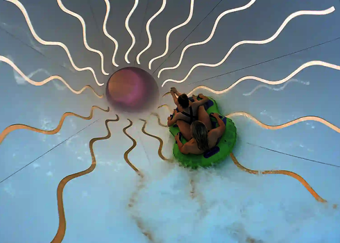 Zwei Personen in einem grünen Rutschreifen fahren eine weiße Wasserrutsche mit gewellten Tageslichteffekten.