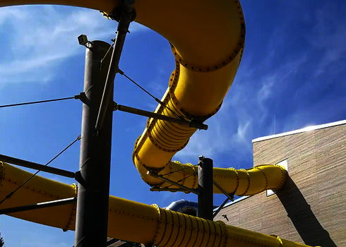 Graue Stahlträger stützen eine gelbe RR1200 Wasserrutsche unter freiem Himmel.