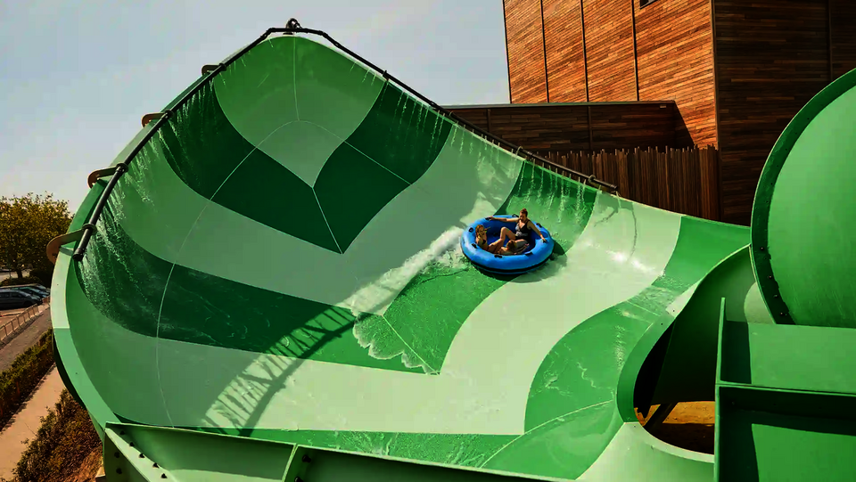 Zwei Personen fahren auf einem Rutschreifen die grüne Lotus Wasserrutsche im Wasserpark.