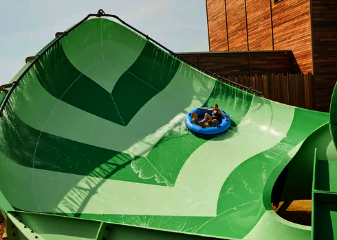 Zwei Personen fahren auf einem Rutschreifen die grüne Lotus Wasserrutsche im Wasserpark.