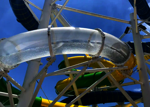 Kurvige Acrylrutsche mit Wasserfluss und bunter Röhrenführung in sonniger Outdoor-Anlage.