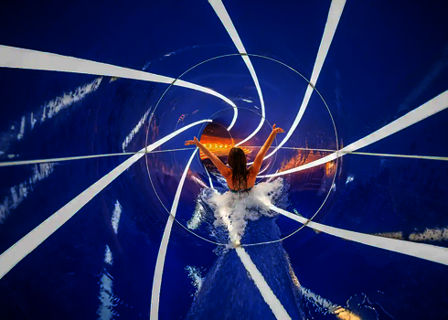 Frau rutscht mit erhobenen Händen durch eine blaue Wasserrutsche mit parallel laufenden Daylights.