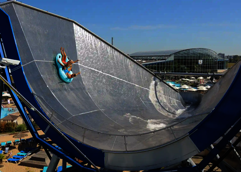 Zwei Personen in blauen Rutschreifen im Urknall, ein großes Glasgebäude im Hintergrund.
