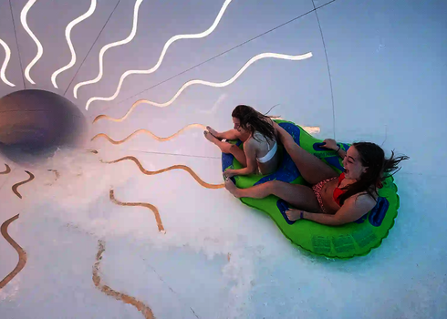 Zwei Frauen rutschen auf einem grünen Rutschreifen in einer weißen Wasserrutsche mit Daylight Effekten.