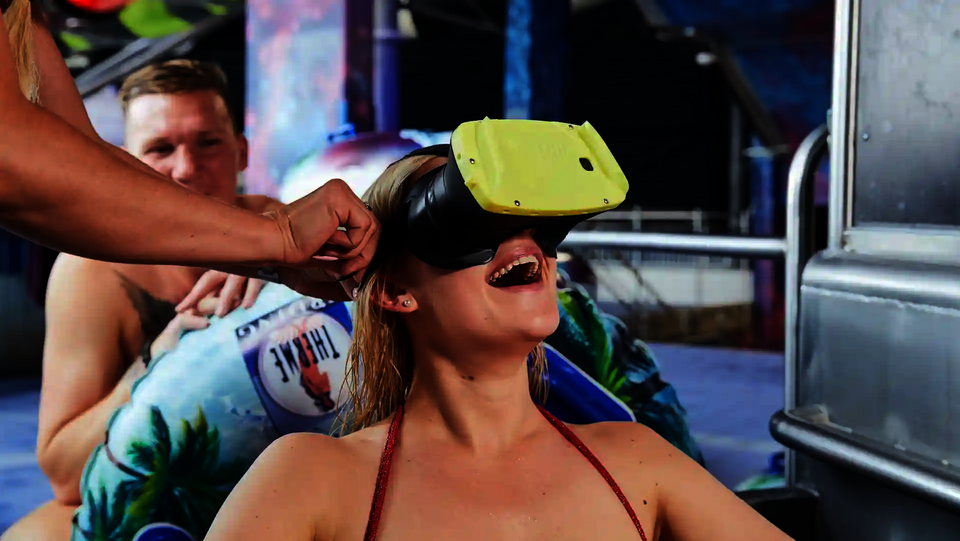 Frau trägt lachend eine VR-Brille, im Hintergrund sitzt ein Mann.