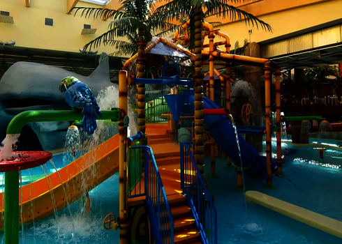 Wasserspielbereich für Kinder in einem Hallenbad mit Palmen und bunten Rutschen.