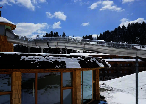 Edelstahlrutsche WR1040 mit Schneebedeckung auf einem Hoteldach in den Bergen.