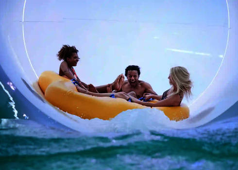 Vier Personen in gelbem Reifenboot rutschen lachend durch eine helle Röhrenrutsche.