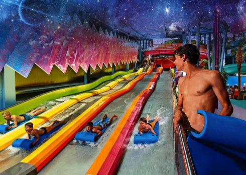 Bunter Indoor Wasserpark mit mehreren Kindern auf Rutschmatten, die auf einem Matracer rutschen.