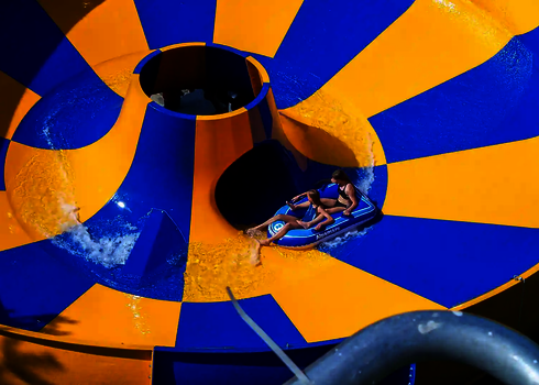 Blick von oben auf eine gelb blaue Raft Bowl Wasserrutsche mit zwei Personen im Rutschreifen.