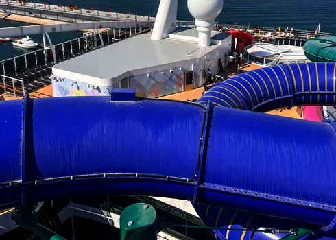 Deck eines Kreuzfahrtschiffes mit dem Ozean im Hintergrund und einer blauen Röhrenrutsche im Vordergrund.