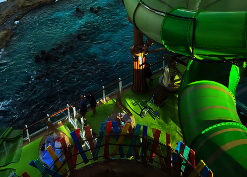 Grüne Röhrenrutsche mit glatter Außenfläche über einem Deck mit Blick aufs Meer.