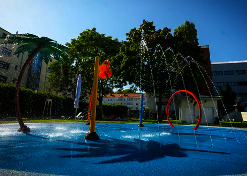 Wasserspielplatz mit Wie-Spray Elementen Palme, Blume und Sprühring in Hotelumgebung.
