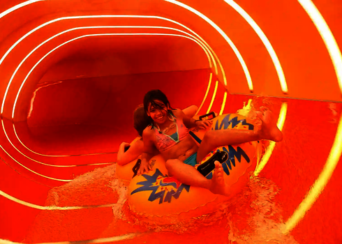 Mädchen mit Begleitung rutscht auf gelbem Reifen durch die beleuchtete Family Twister Wasserrutsche.