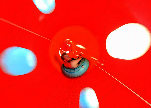 Eine rote Wasserrutsche von innen, mit einer Person auf einem blauen Rutschreifen.