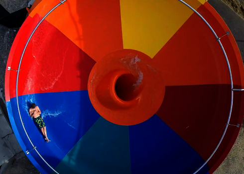 Obenansicht einer bunten Body Bowl Wasserrutsche, in der eine Person mit Badebekleidung rutscht.