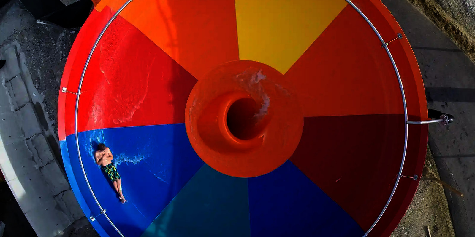 Obenansicht einer bunten Body Bowl Wasserrutsche, in der eine Person mit Badebekleidung rutscht.
